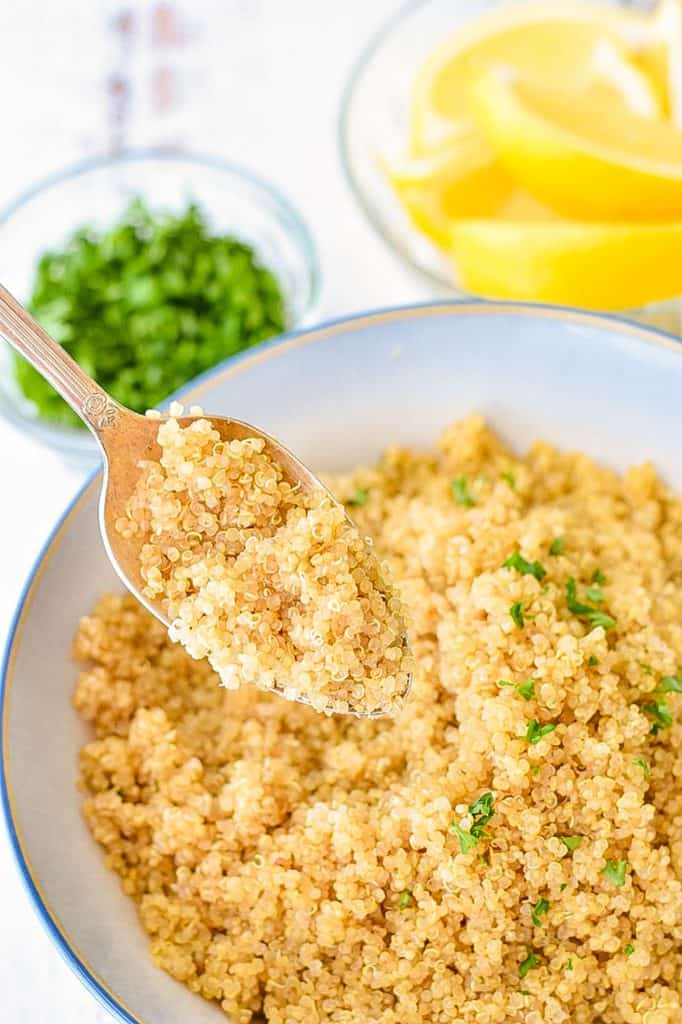 a spoonful of cooked low fodmap white quinoa over a blue and white bowl of quinoa