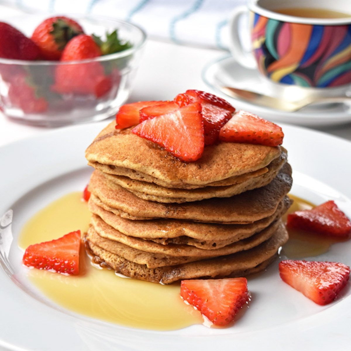 a stack of tigernut flour pancakes topped with strawberries and maple syrup on a white plate