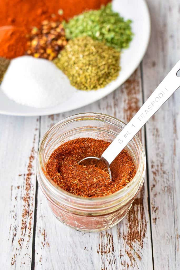 low fodmap cajun spice blend in a clear jar with a teaspoon in front of a plate of individual spices