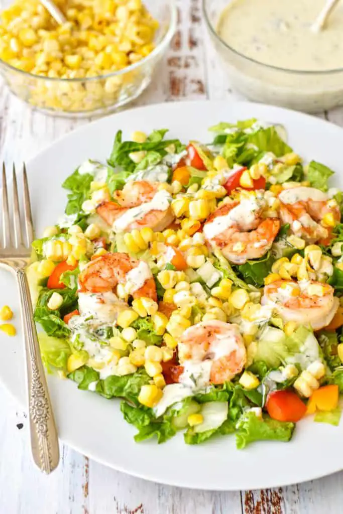 side lit angle shot of low FODMAP summer detox salad with corn, shrimp and dairy-free ranch dressing on a white plate with a fork