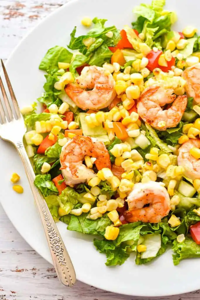 close up shot of low fodmap salad with grilled shrimp, corn, bell pepper, and lettuce on a white plate with a fork