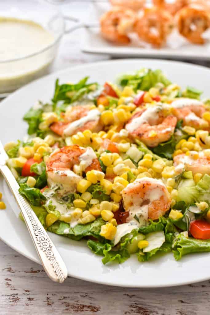 back lit side angle shot of low FODMAP summer detox salad with corn and shrimp dressed in ranch dressing on a white plate with a fork