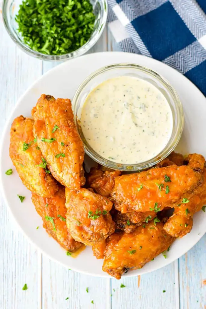 overhead shot of low fodmap air fryer buffalo chicken wings on a white plate with a bowl of ranch dressing and garnished with chopped parsley
