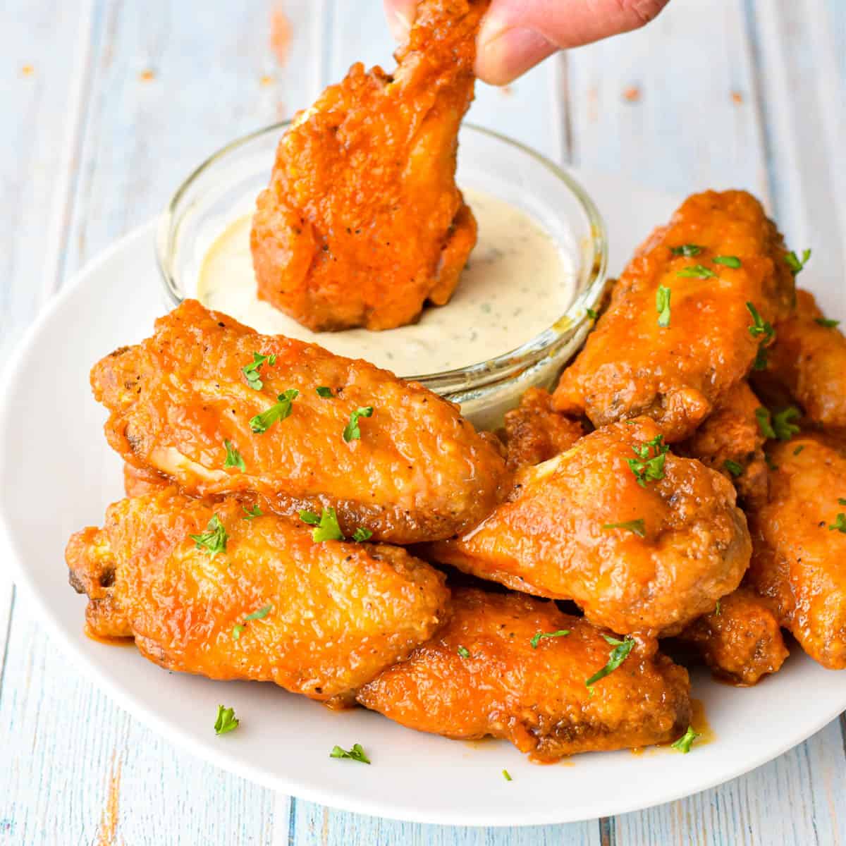 a buffalo wing being dipped in ranch dressing on a plate of chicken wings 