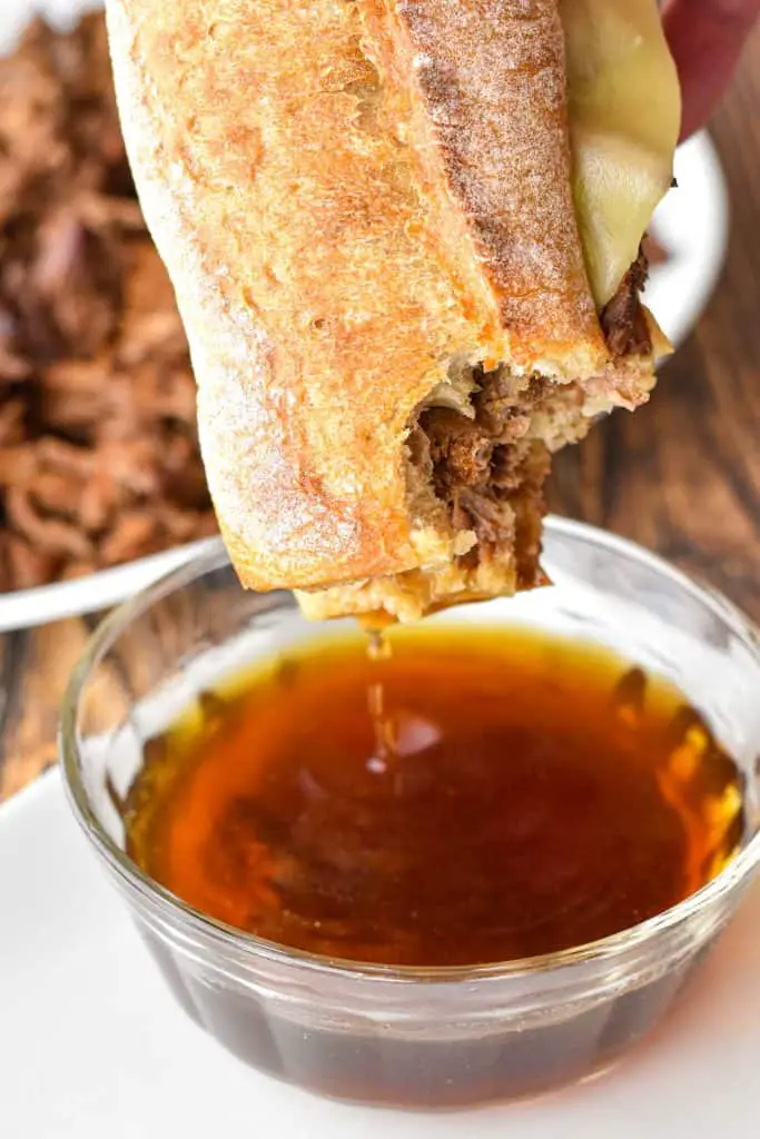a low FODMAP french dip sandwich with a bite taken out dripping over a bowl of au jus