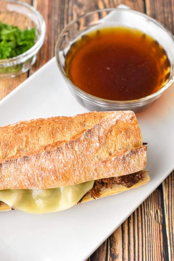 overhead shot of low fodmap beef dip sandwich on a white plate with dipping broth