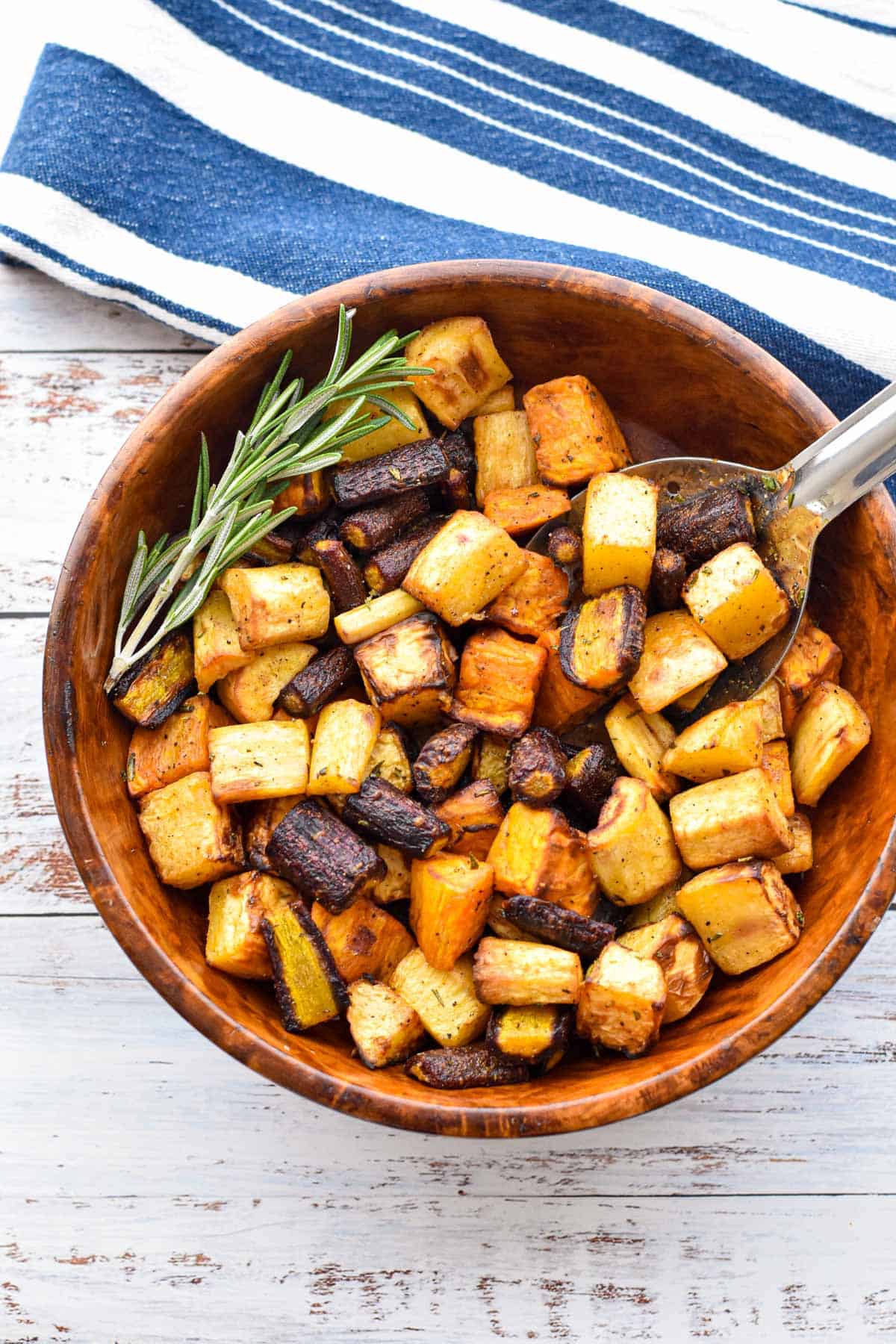 low fodmap air fryer root vegetables in a wooden bowl with a spoon and spring of rosemary