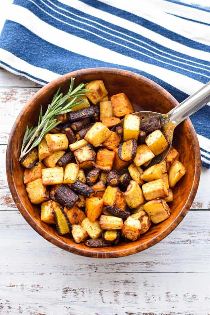 overhead shot of low fodmap air fryer root vegetables in a wood bowl with a silver spoon next to a blue and white striped towel 