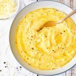 low fodmap polenta garnished with shredded cheese and black pepper in a white, blue rimmed bowl with a spoon