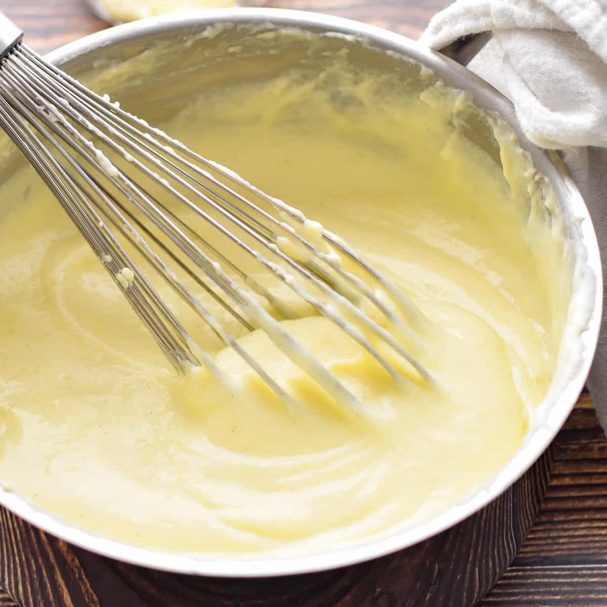 white sauce with a whisk in a silver pot on a wooden background 