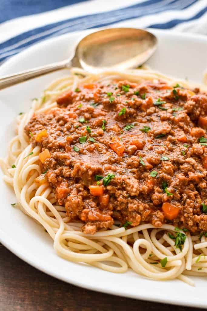 low fodmap spaghetti Bolognese on a white platter with a spoon on a brown background.