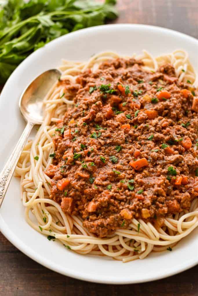 side angle shot of low fodmap spaghetti bolognese on a platter with a spoon in front of a parsley bunch.