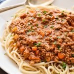 low fodmap Bolognese on top of spaghetti on a white platter with a spoon