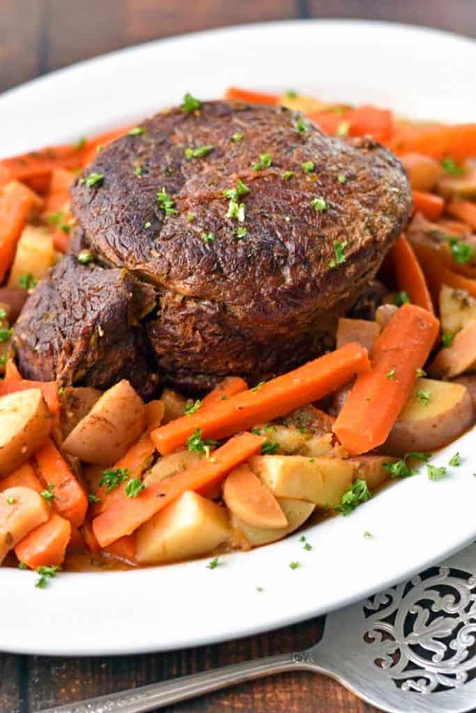 low fodmap beef pot roast, carrots, potatoes and mushrooms on a platter beside a fancy spoon.