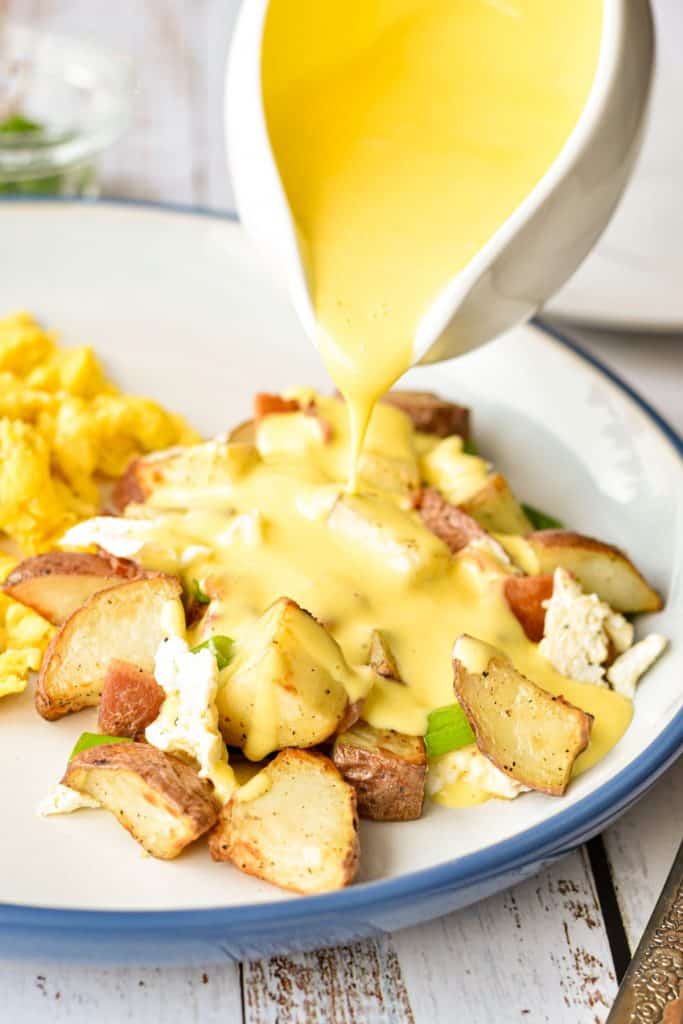 close up shot of low fodmap hollandaise sauce being poured on low fodmap breakfast poutine on a blue and white plate