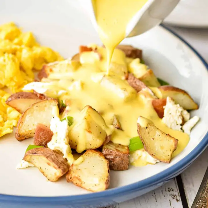 pouring low fodmap hollandaise on top of low fodmap breakfast poutine on a plate.