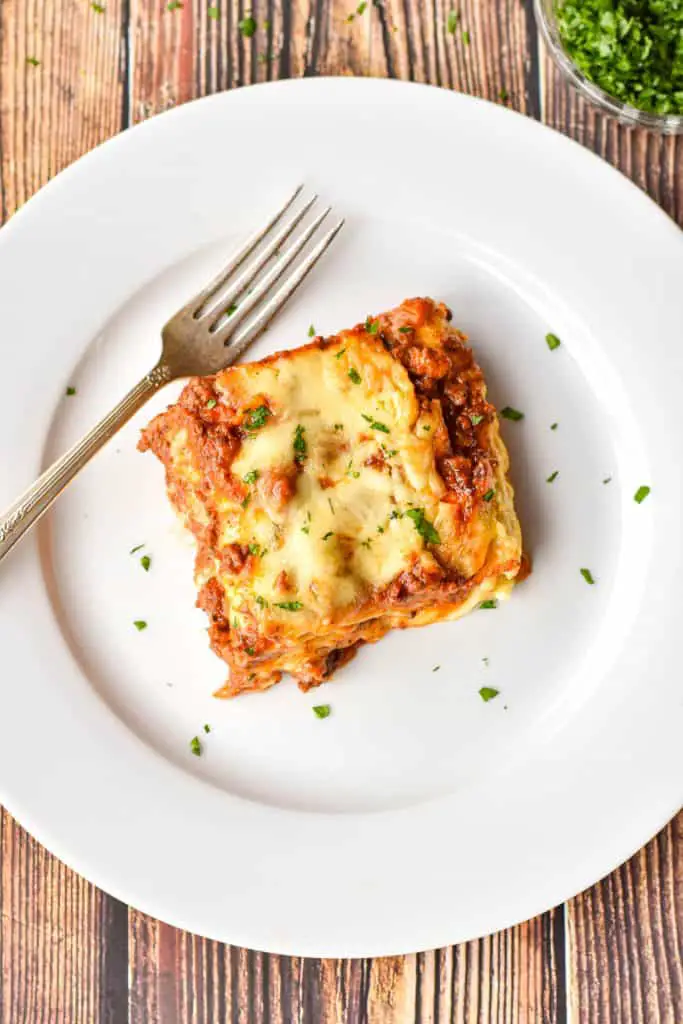 overhead shot of a square piece of gluten-free lasagna on a round white plate with a fork.