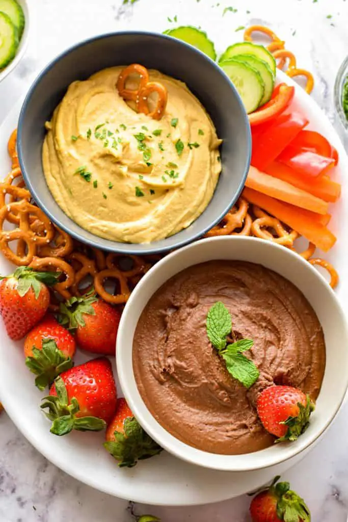 overhead shot of low fodmap hummus - 2 ways (classic and chocolate dessert on a platter with veggies, pretzels and strawberries