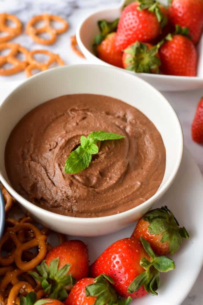 low fodmap chocolate hummus in a white bowl on a platter with strawberries and gluten-free pretzels