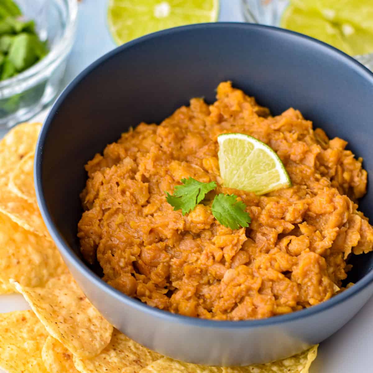 refried beans in a navy blue bowl on a plate with tortilla chips