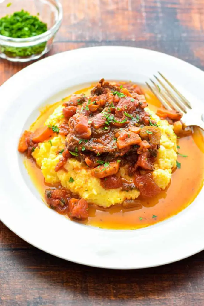 a slice of low fodmap italian pot roast on top of polenta on a white plate with a fork