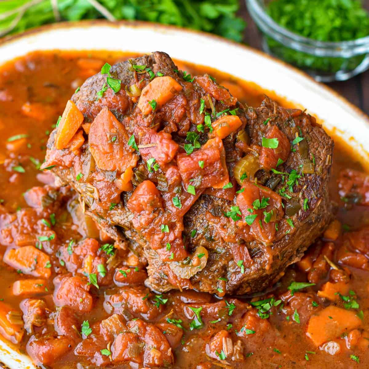 italian pot roast covered in tomato sauce on a platter in front of parsley