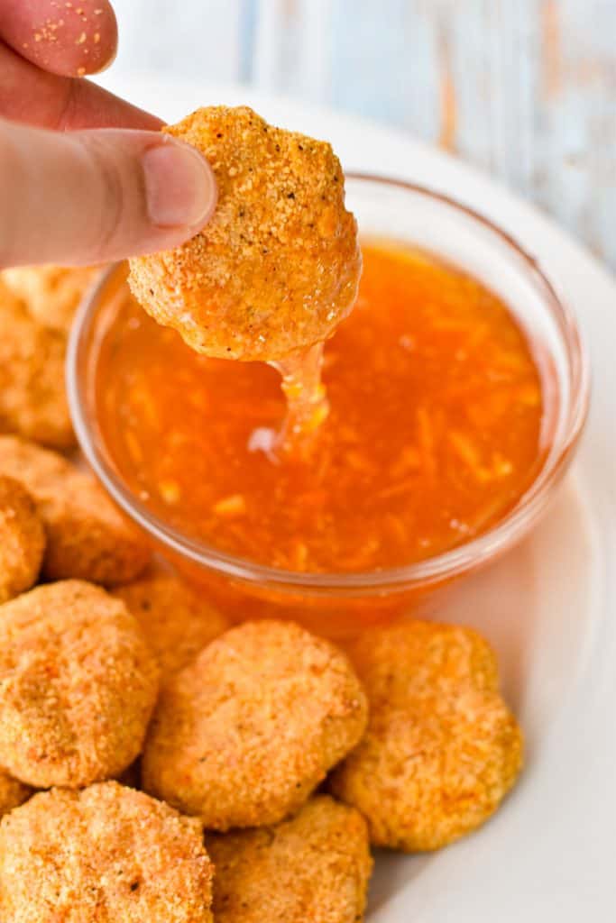 a hand dipping a low fodmap chicken nugget in a bowl of low fodmap sweet and sour dipping sauce