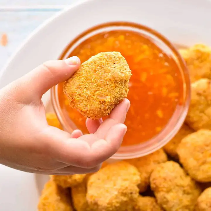 a hand holding a low fodmap chicken nugget over a bowl of sweet and sour sauce