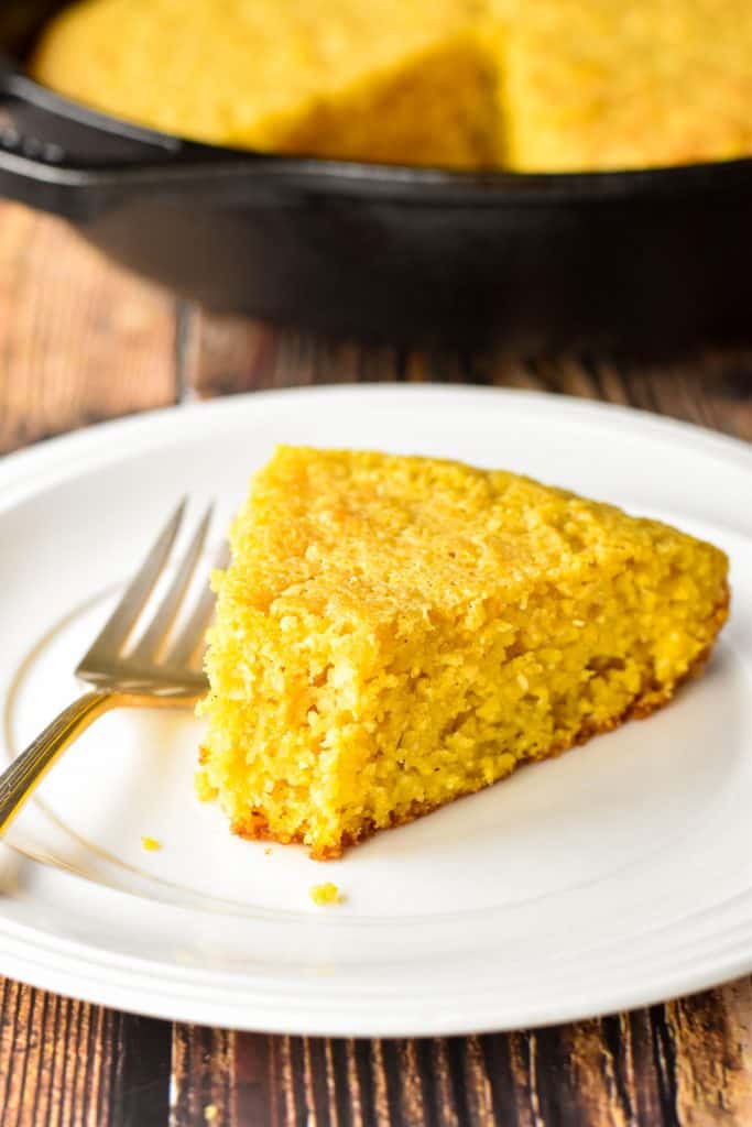 close up shot of a piece of low fodmap cornbread on a white plate with a bite taken out of it next to a fork