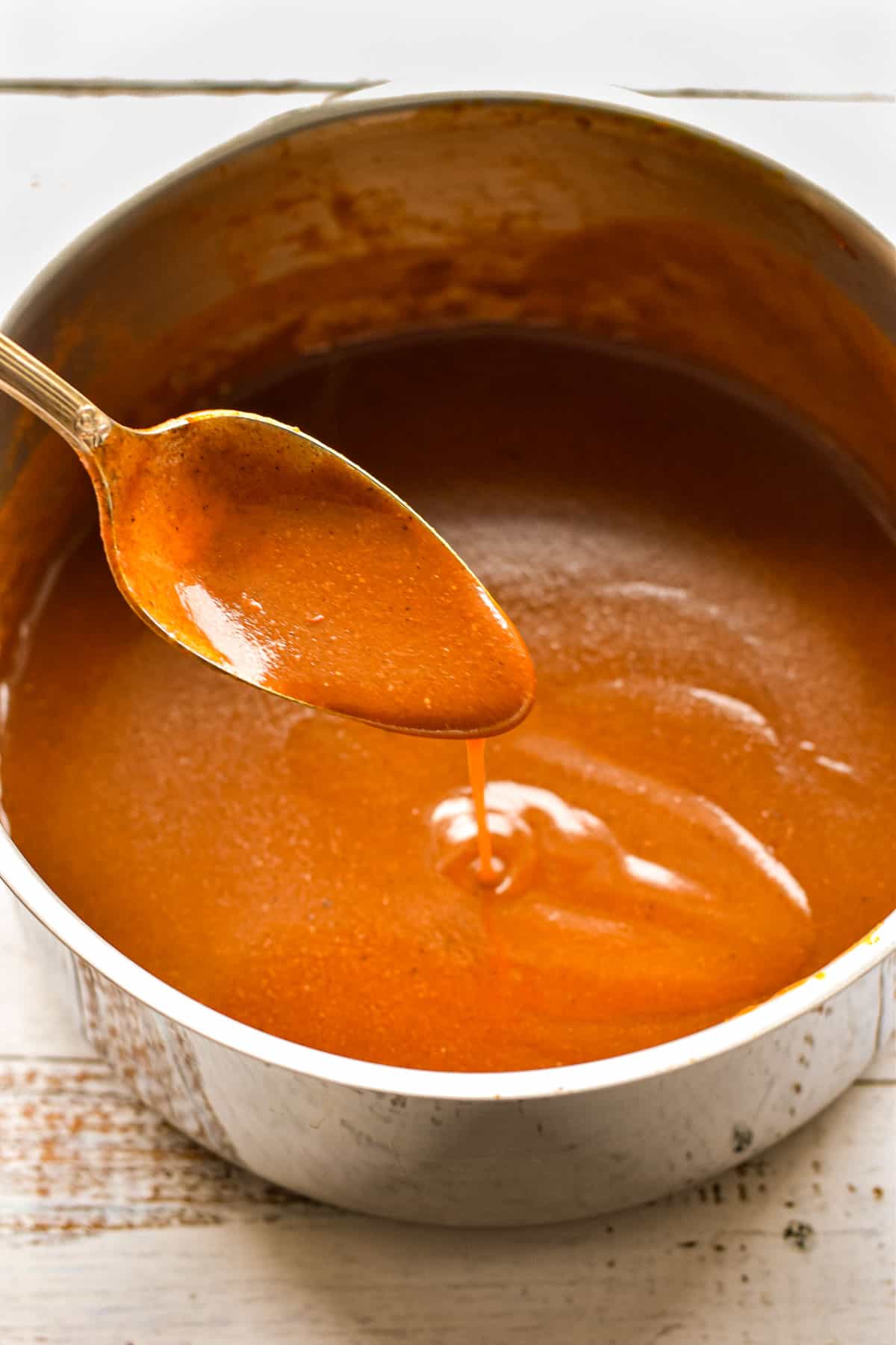 a spoon dripping low fodmap enchilada sauce into a saucepan