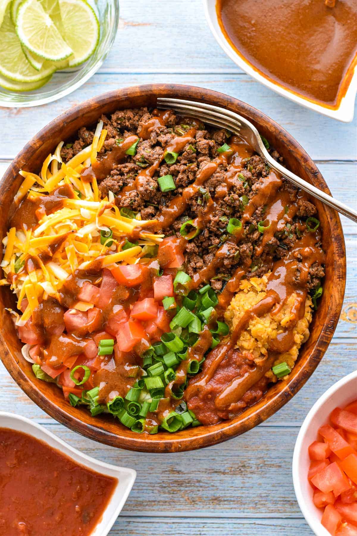 close up shot of a low fodmap wet burrito bowl containing ground beef, shredded cheese, chopped tomatoes and scallions, salsa and refried beans and topped with enchilada sauce