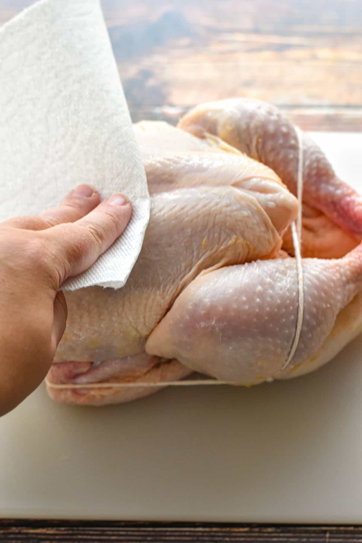 a hand drying a trussed raw whole chicken with paper towels