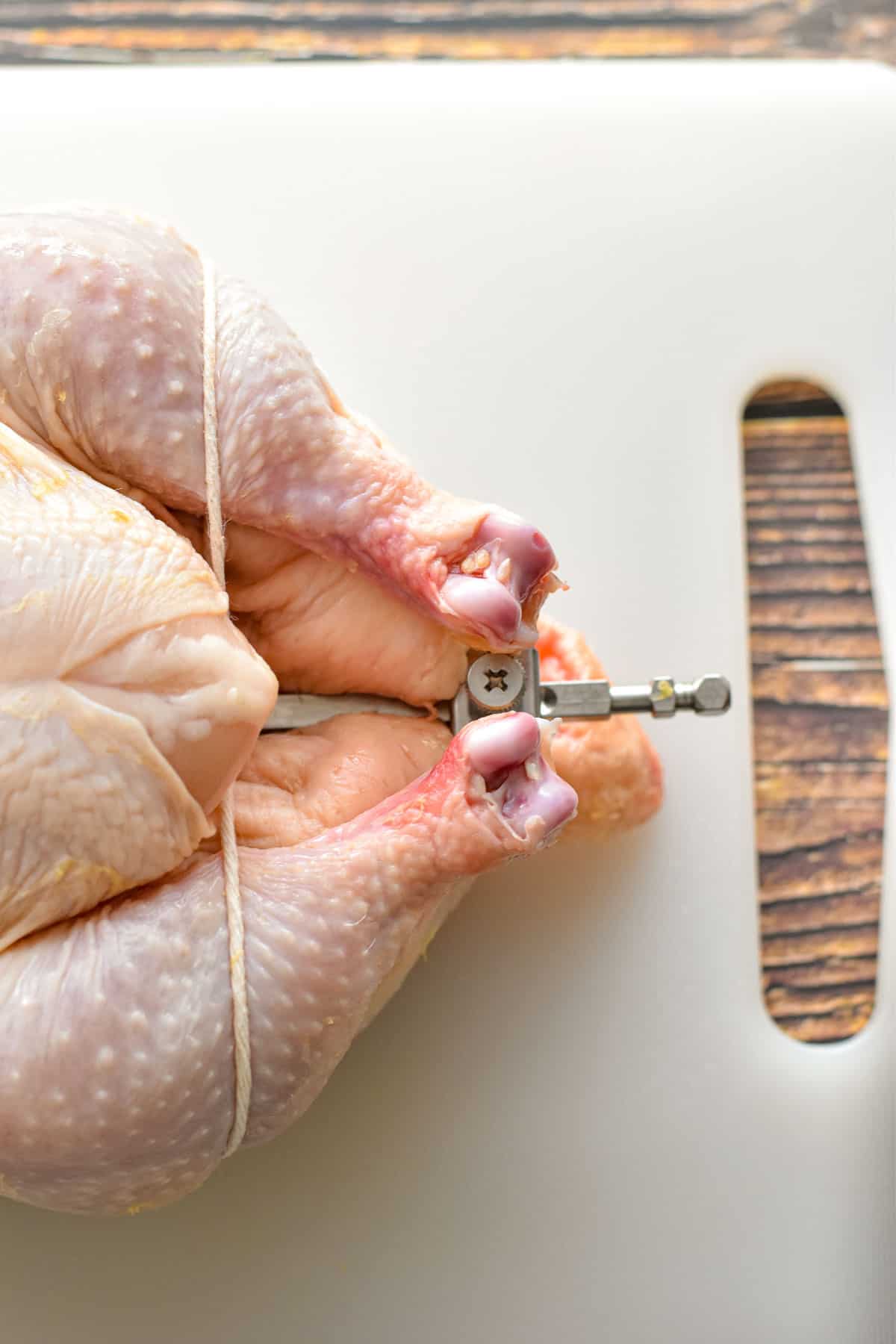 overhead shot of the leg end of a raw whole chicken with a rotisserie spit inside