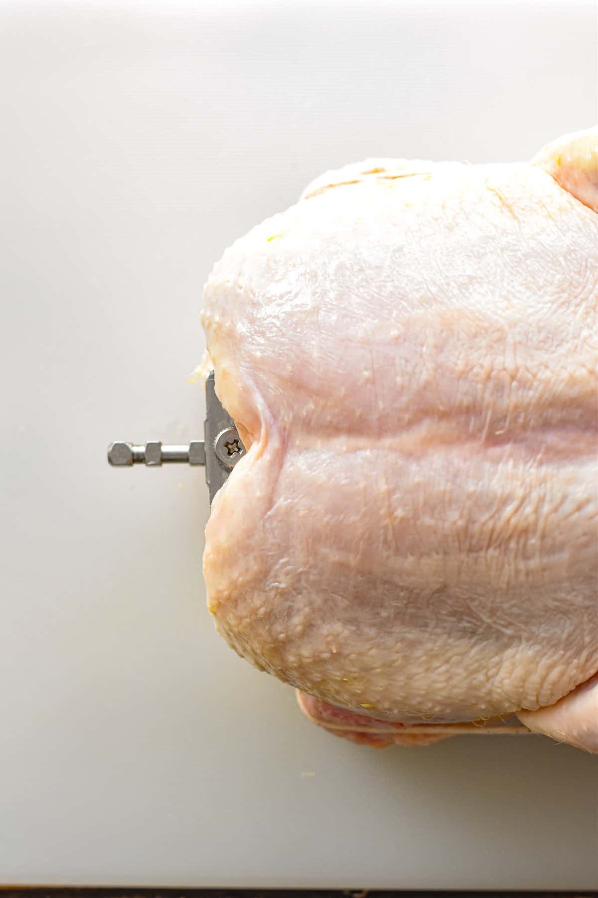 overhead shot of the top end of a raw whole chicken with a rotisserie spit in its internal cavity