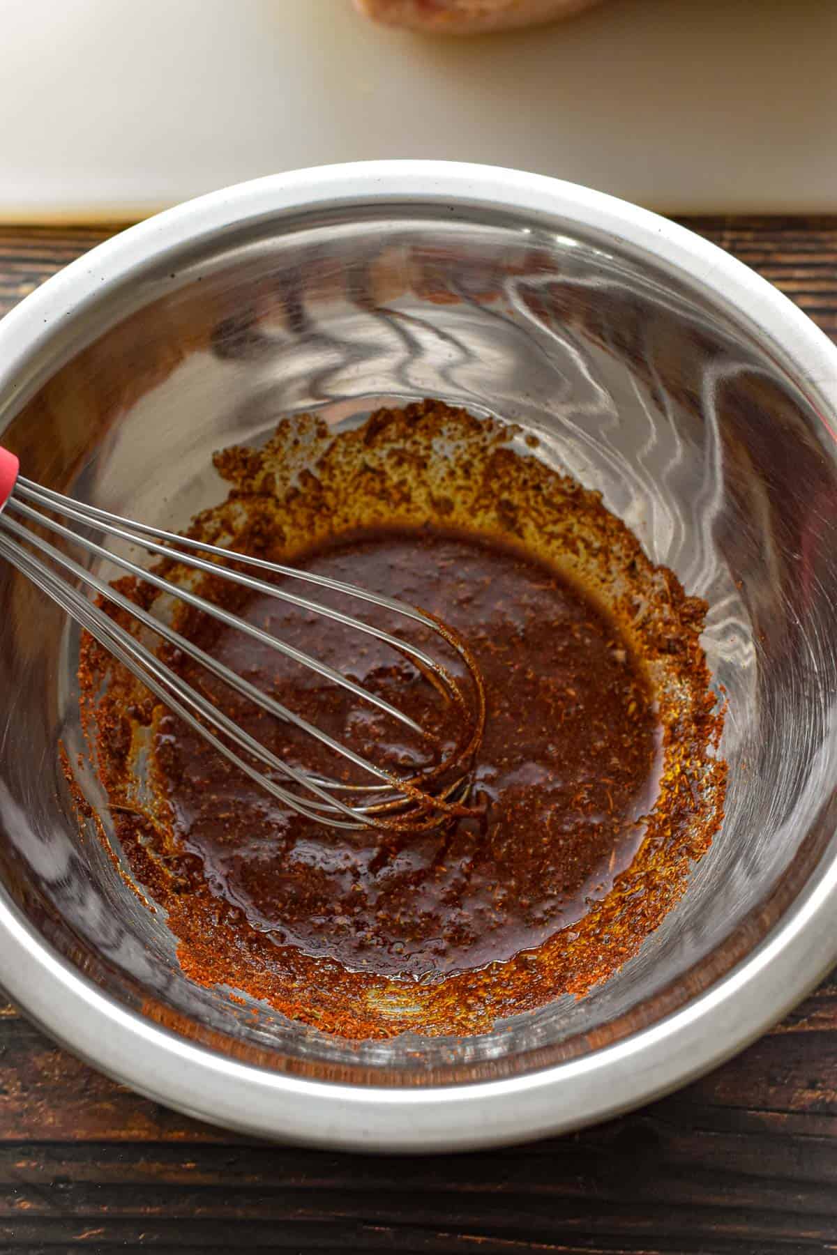 whisking together oil and rotisserie chicken seasoning in a metal bowl