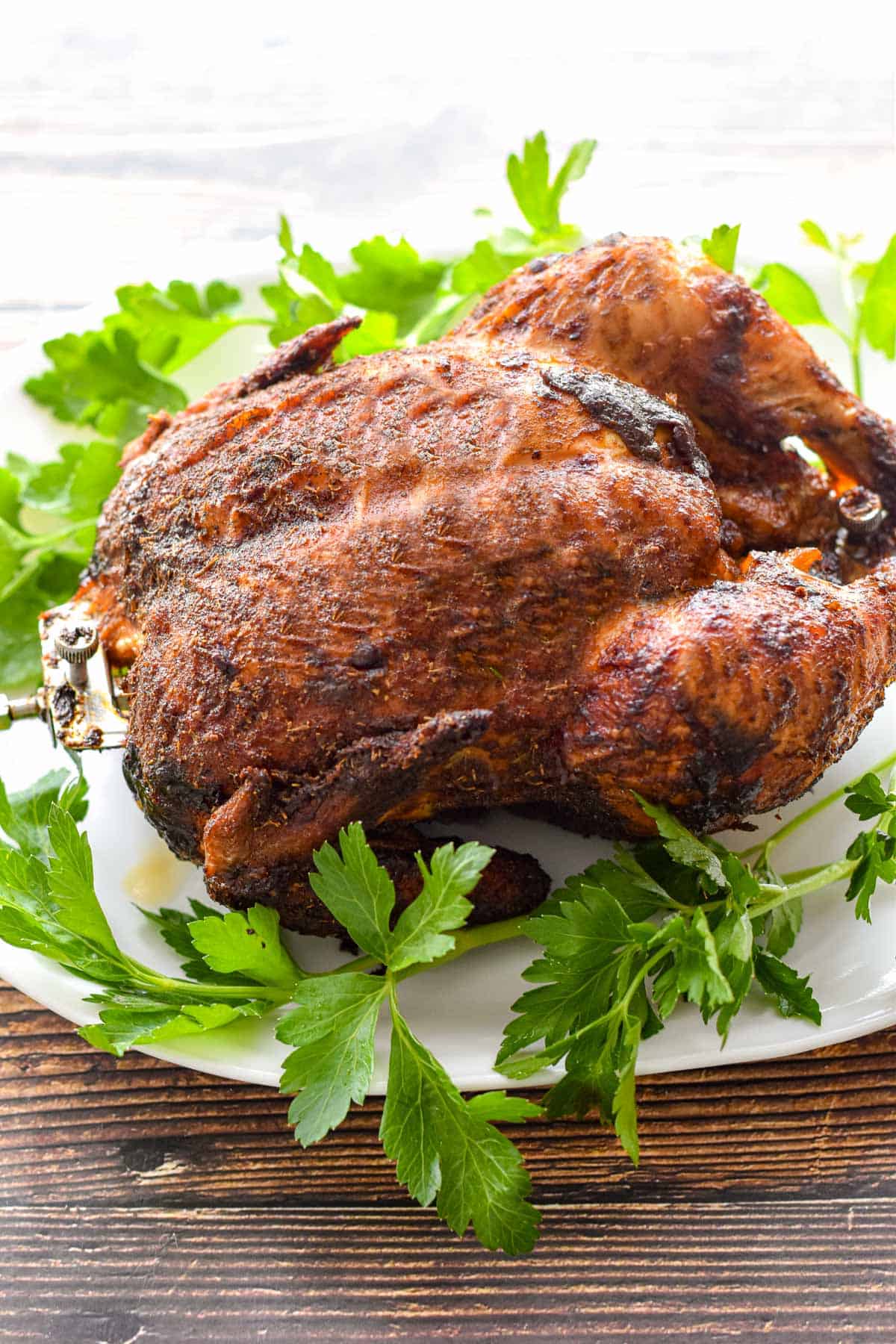 side view of a cooked low fodmap rotisserie chicken resting on a white platter with parsley
