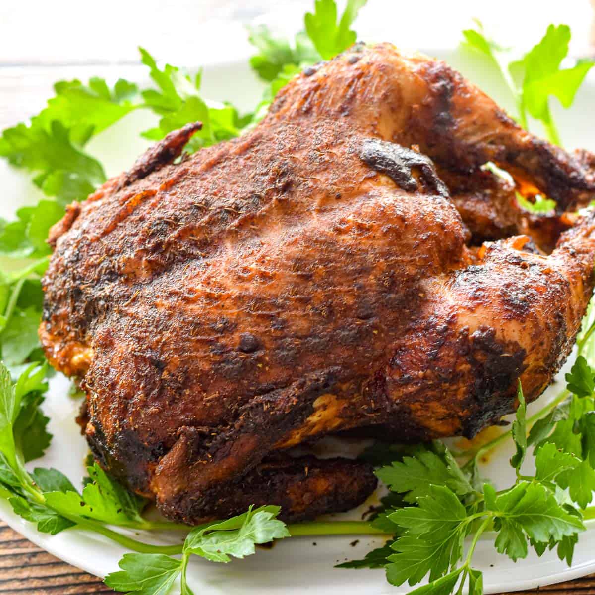 a cooked rotisserie chicken on a white platter surrounded by parsley