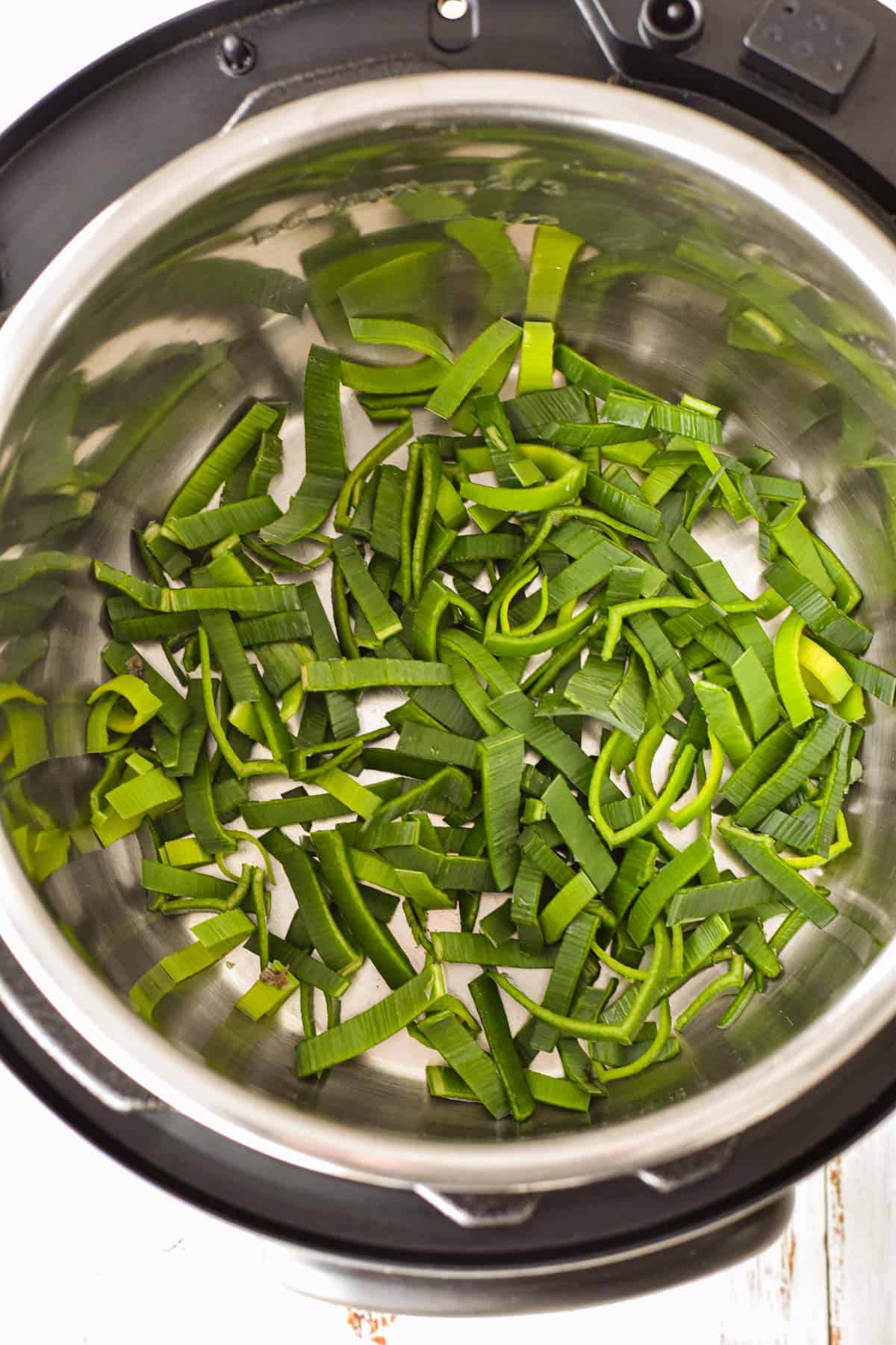 sliced green leek leaves in the bottom of an instant pot