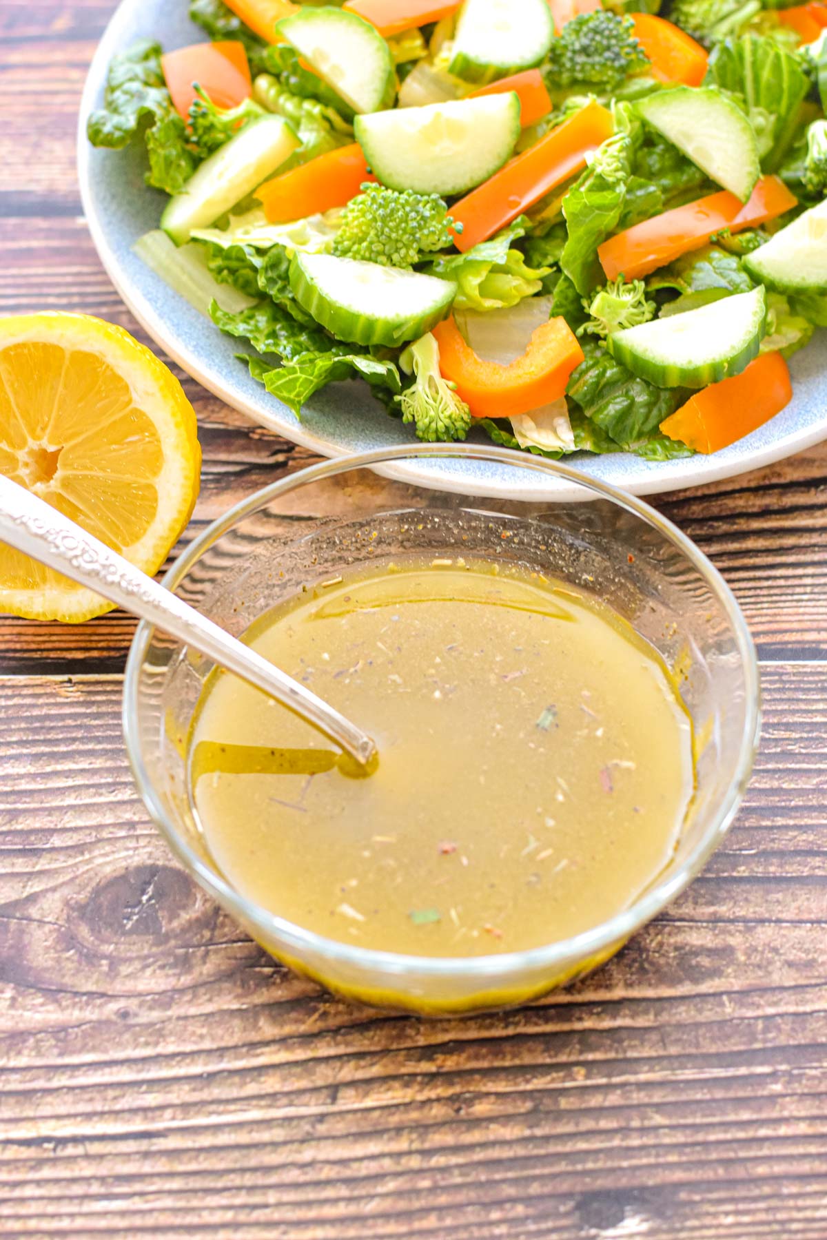 low fodmap italian salad dressing in a glass bowl with a spoon in front of a salad and sliced lemon