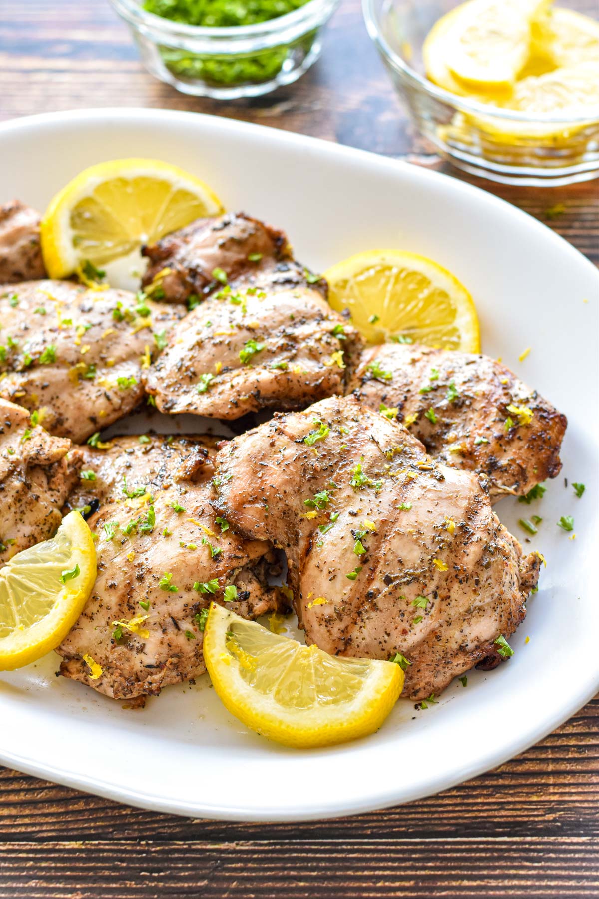 side angle shot of boneless skinless marinade low fodmap grilled chicken thighs on a white platter with lemon slices