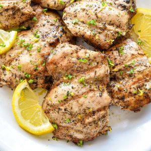 low fodmap marinated chicken thighs on a white platter with lemon slices
