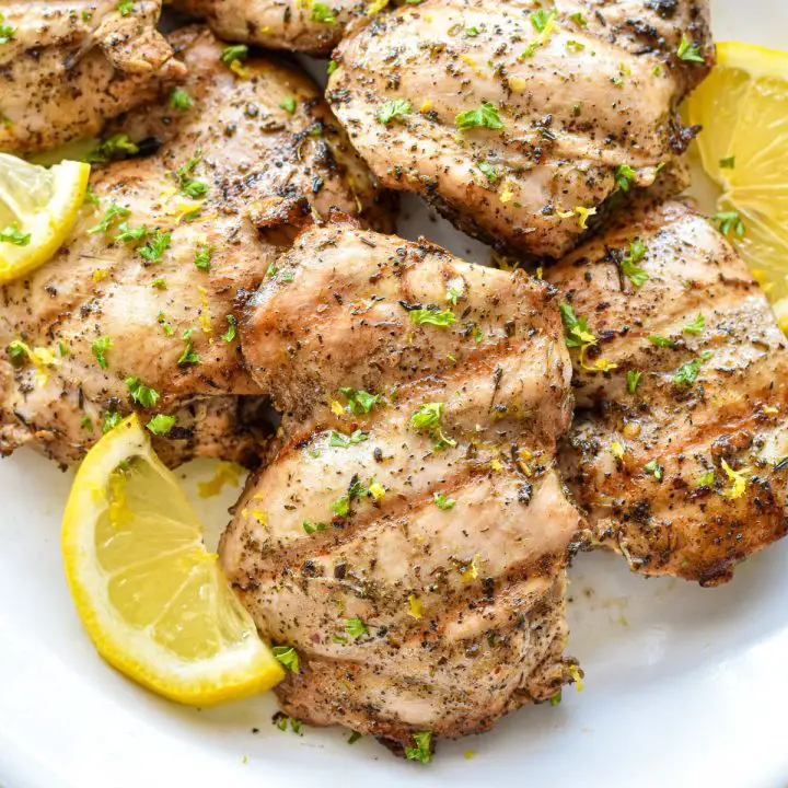 low fodmap marinated chicken thighs on a white platter with lemon slices.
