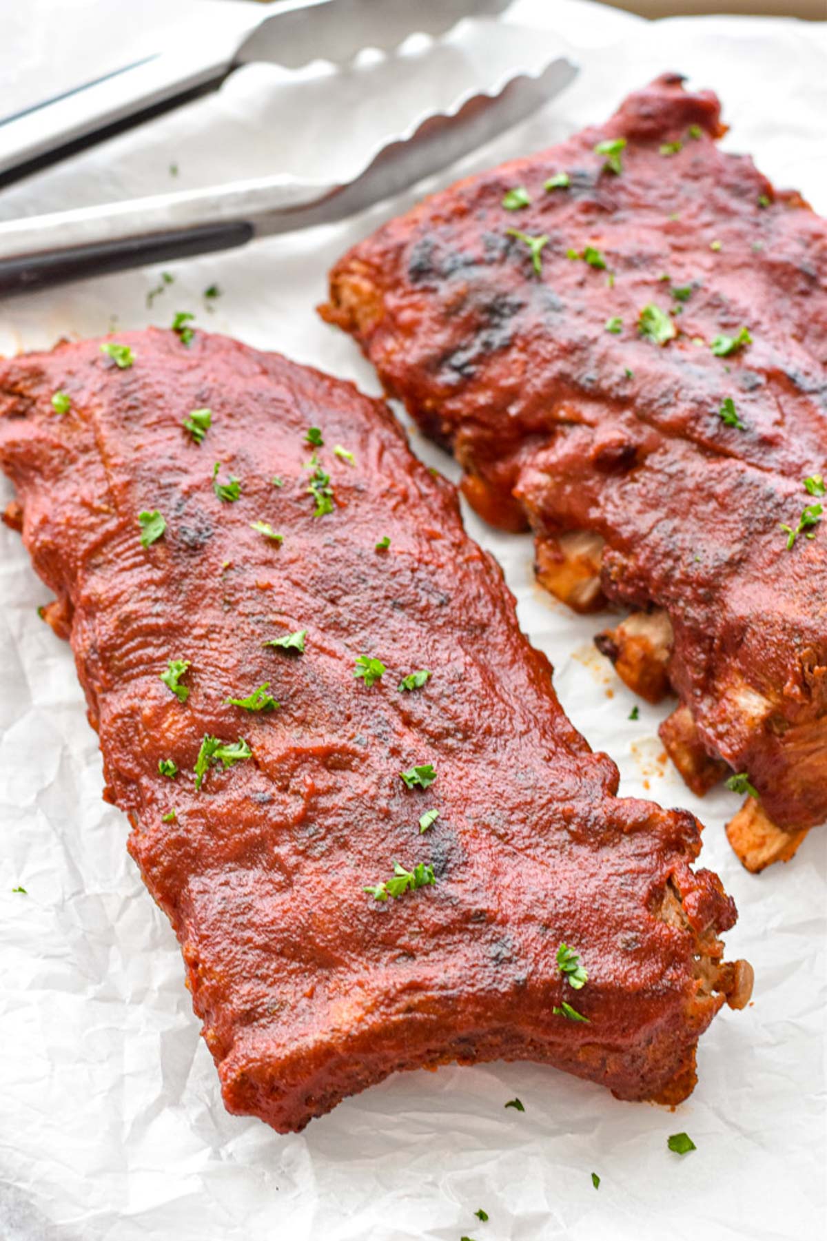 Low FODMAP ribs on parchment paper garnished with chopped parsley in front of tongs