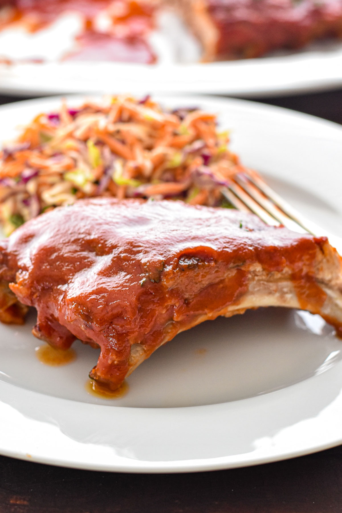 low fodmap pork ribs covered in BBQ sauce on a white plate with a side of coleslaw and a fork.