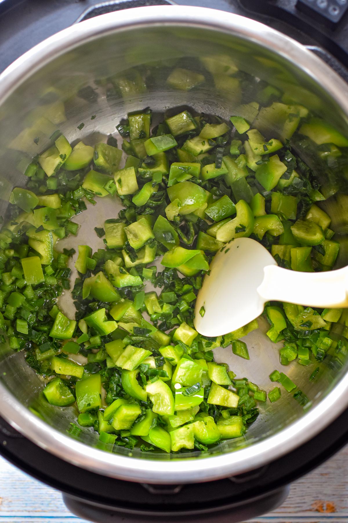 chopped green bell pepper, jalapeño, and leek being sautéed in the Instant Pot with a plastic spoon