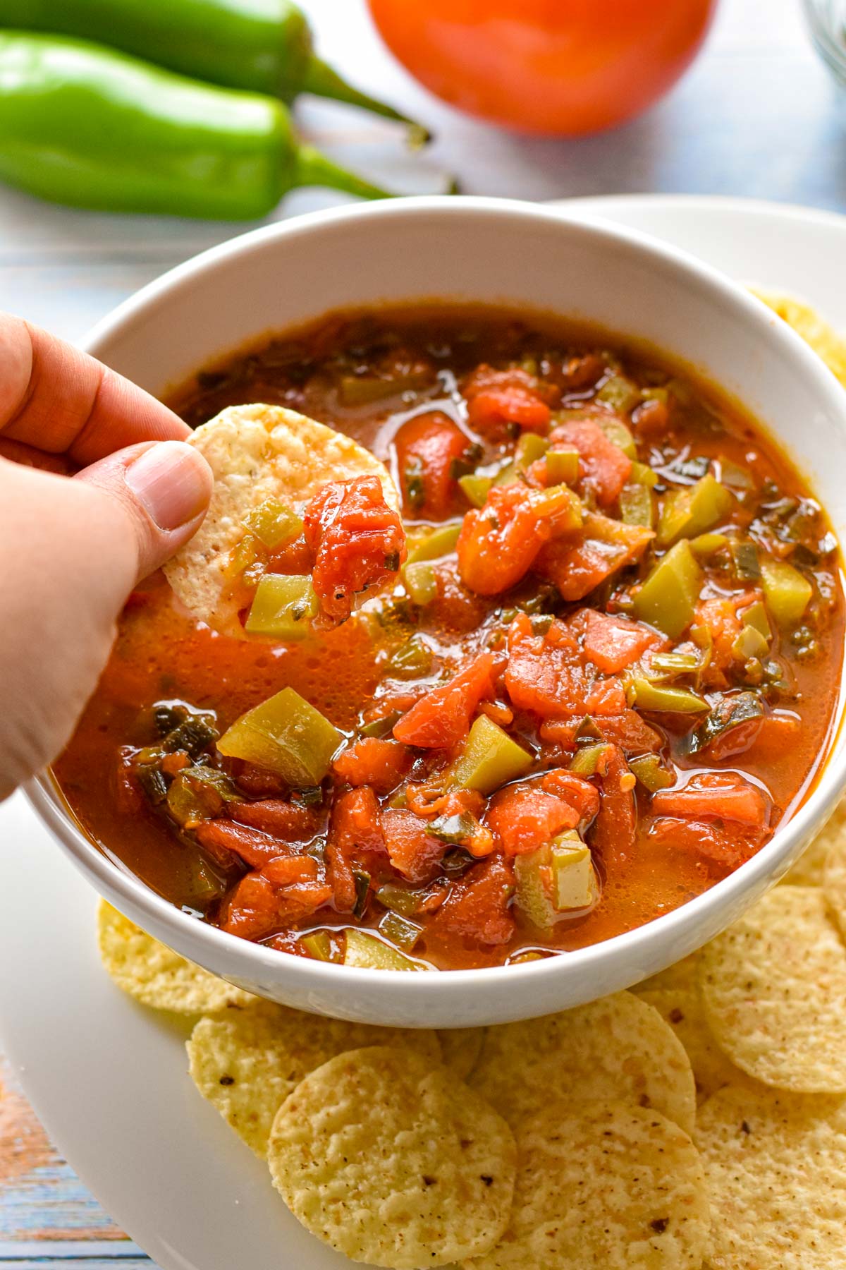dipping a tortilla chip into a white bowl of low fodmap salsa on a plate surrounded by more chips