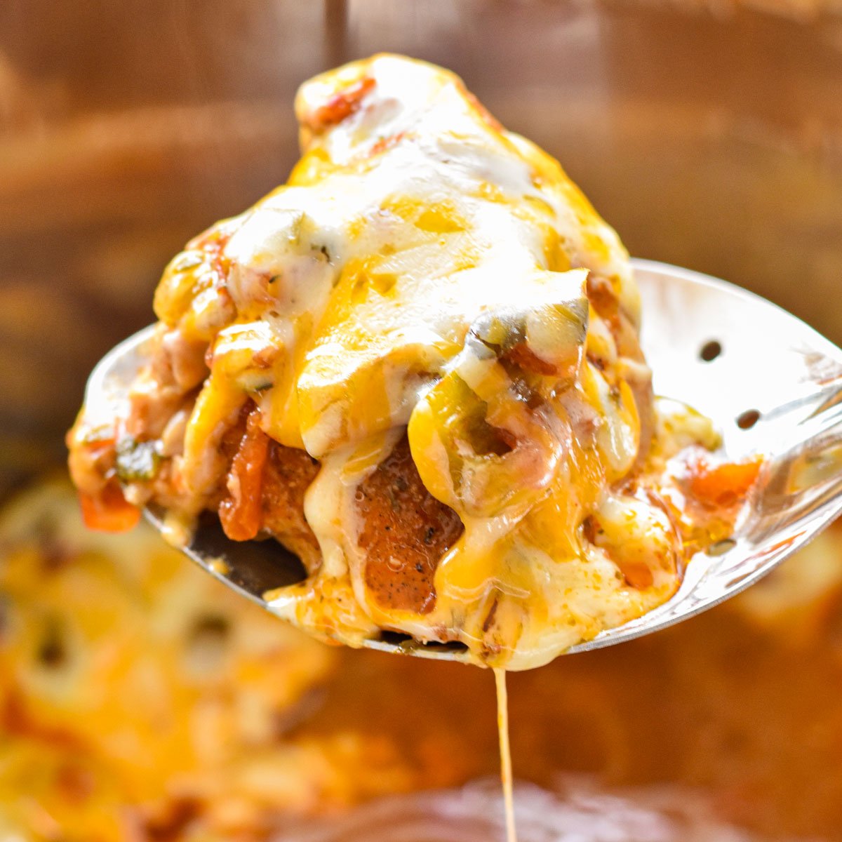 a spoon holding a chicken thigh smothered in salsa and melted cheese 