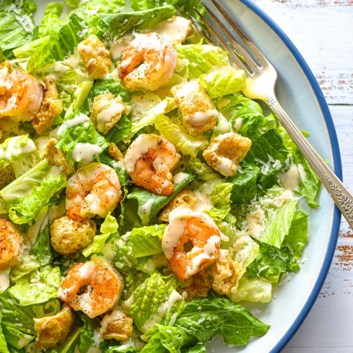 low fodmap Caesar salad with shrimp pork rind croutons and dressing on a blue and white plate
