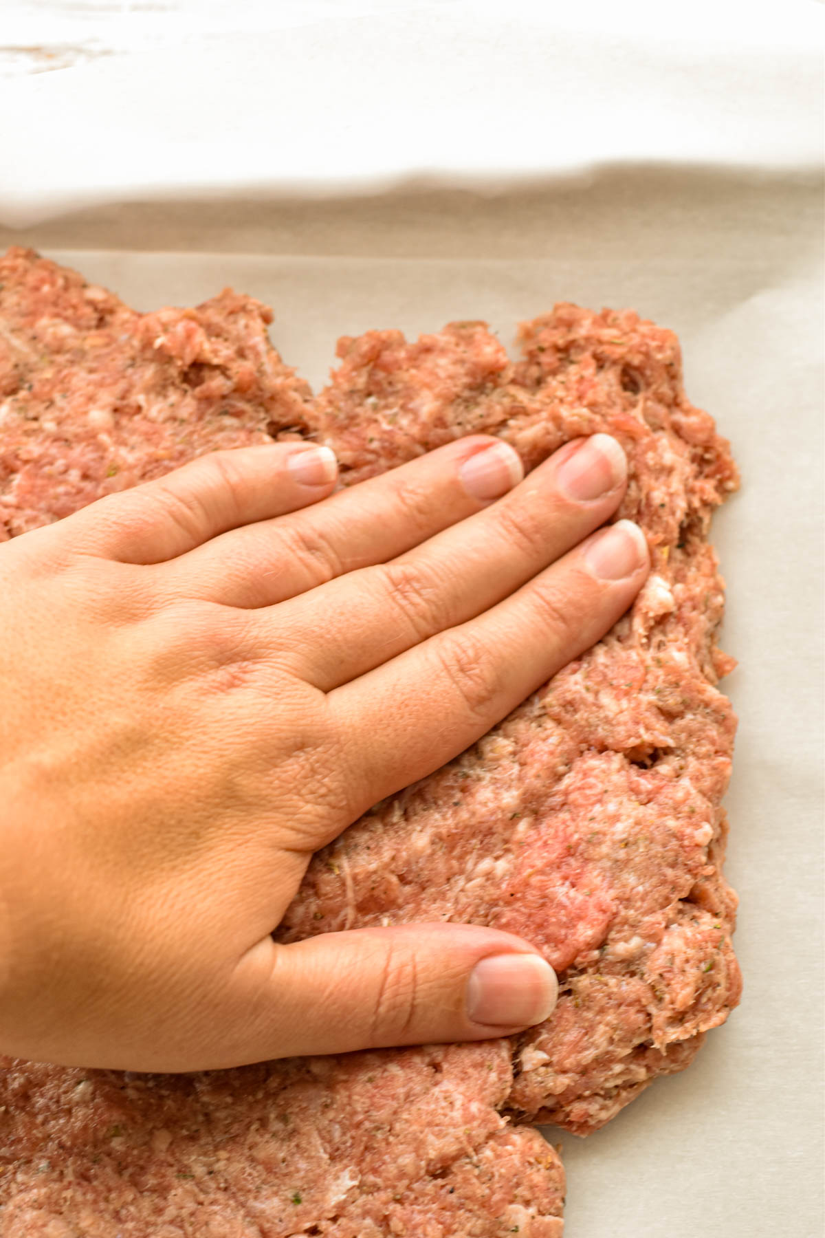 process shot of a hand spreading low fodmap meatza "dough" to the edges of a baking sheet covered with parchment paper