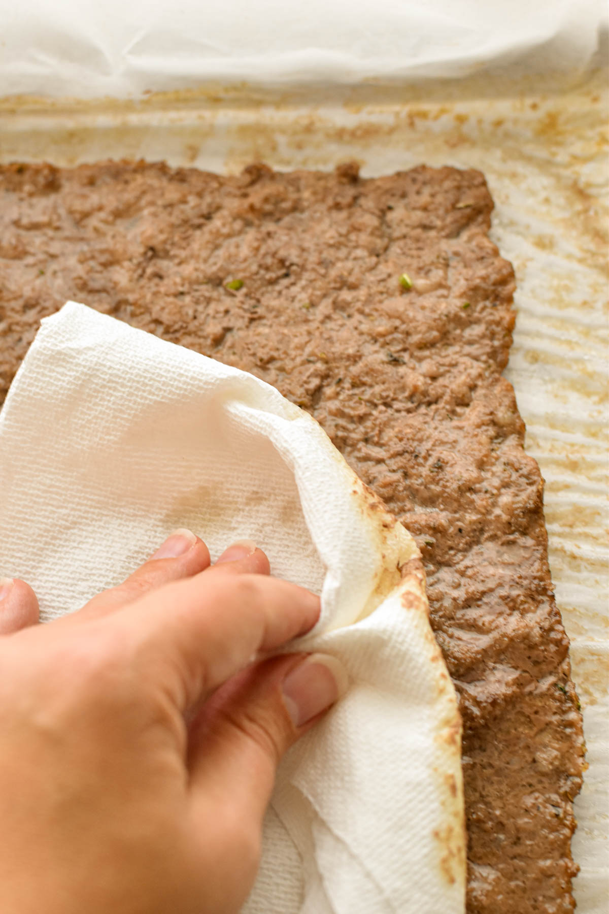 process shot of a hand blotting the low fodmap meatza crust dry with folded over paper towels